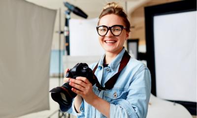 Uma fêmea fotógrafo usando óculos e uma camisa azul segurando uma câmera DSLR