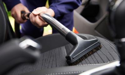 Car valeter vacuuming a seat of a car
