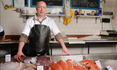 Portrait of salesman in apron offering female customer fresh fish