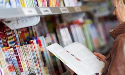 Woman in leather jacket reading book with other books in background